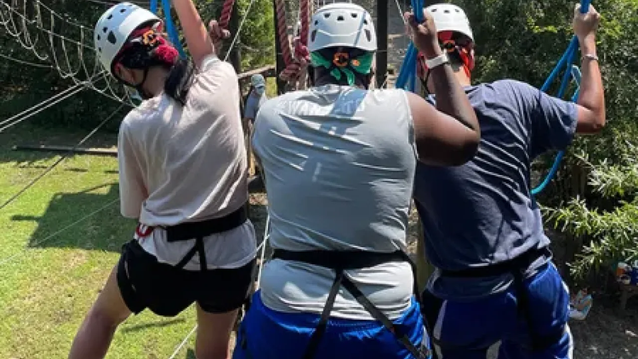 Three people 30 feet in the air walk across cables while wearing safety equipment