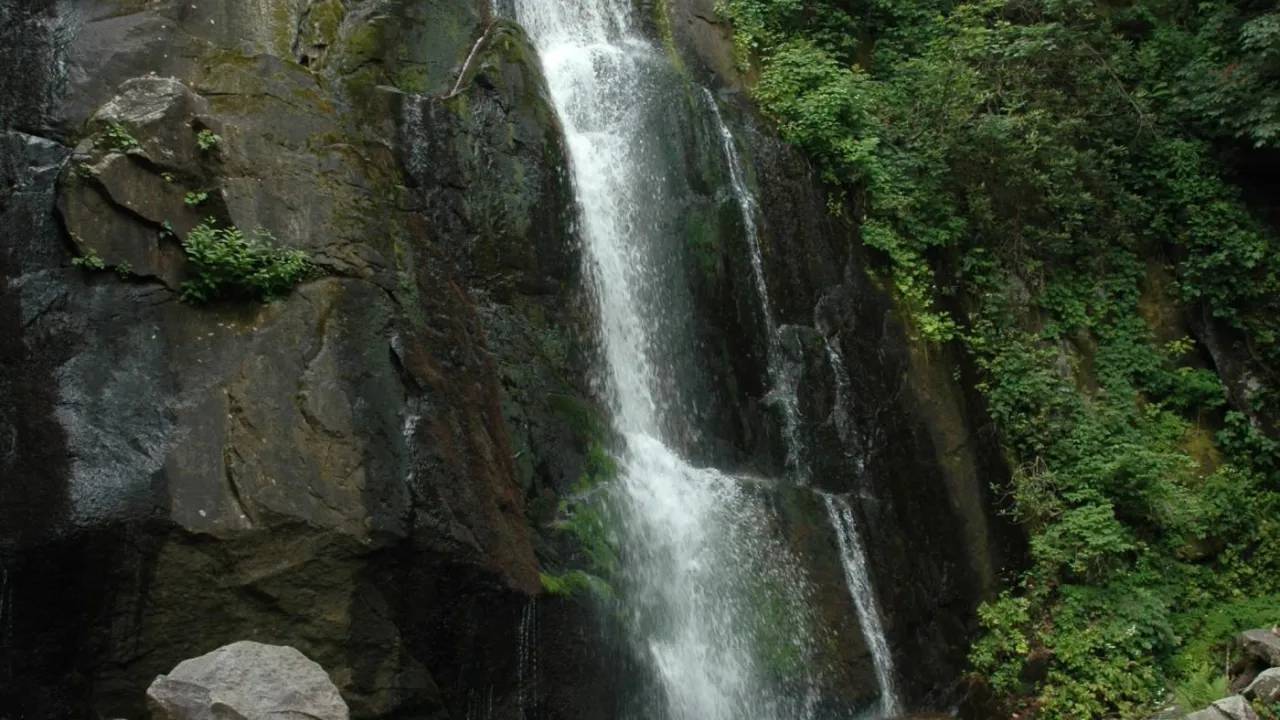 Cascading waterfall surrounded by dark rock and greenery