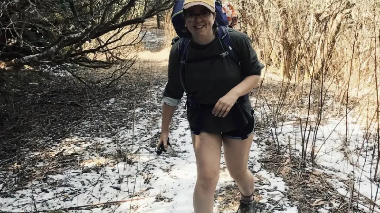 Female presenting person walking toward the camera, hiking on snow strewn trail