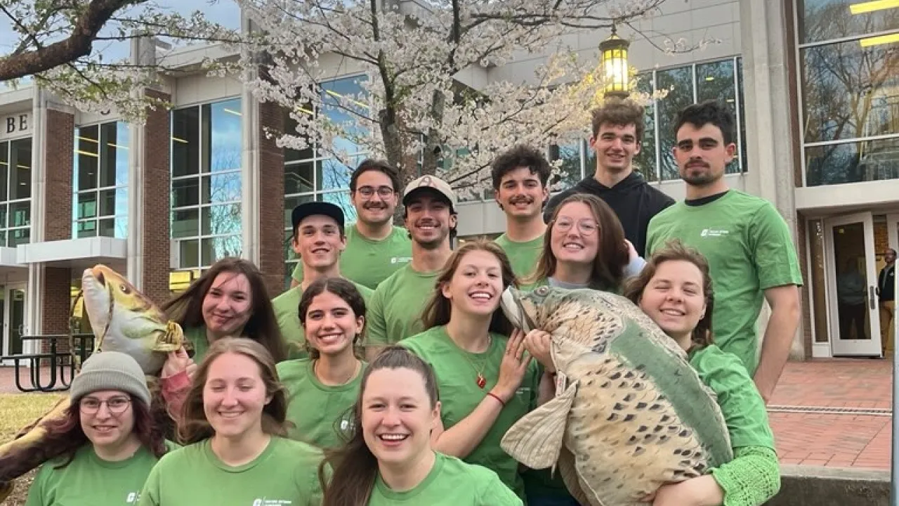 Group of student smiling at the camera holding stuffed fish.