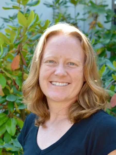 Female presenting person in front of green bushes