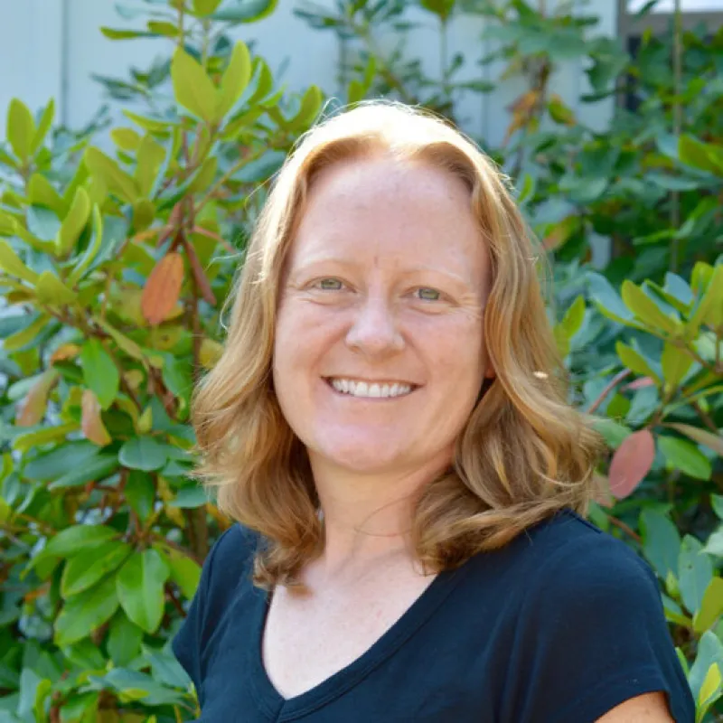 Female presenting person in front of green bushes